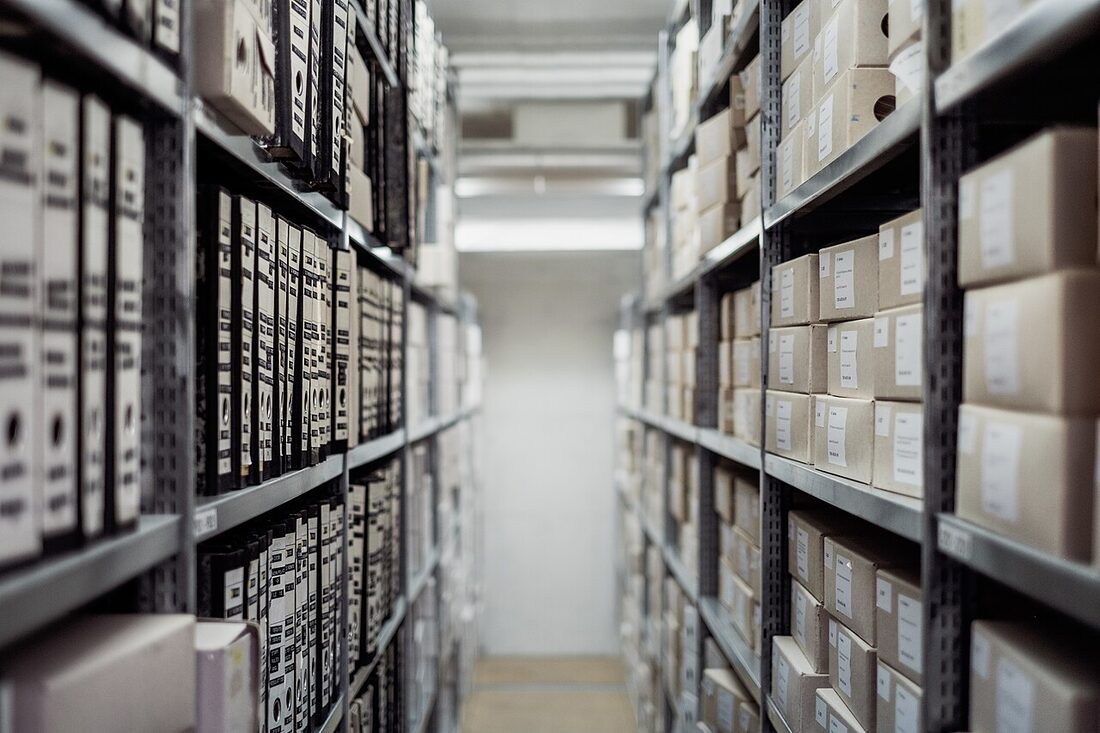 Deux rangées d'étagères d'archives remplies de boîtes et de classeurs étiquetés